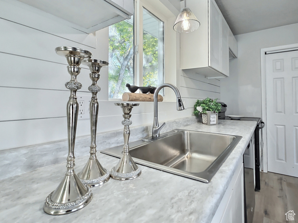 Kitchen featuring a sink, white cabinets, light countertops, wood finished floors, and pendant lighting