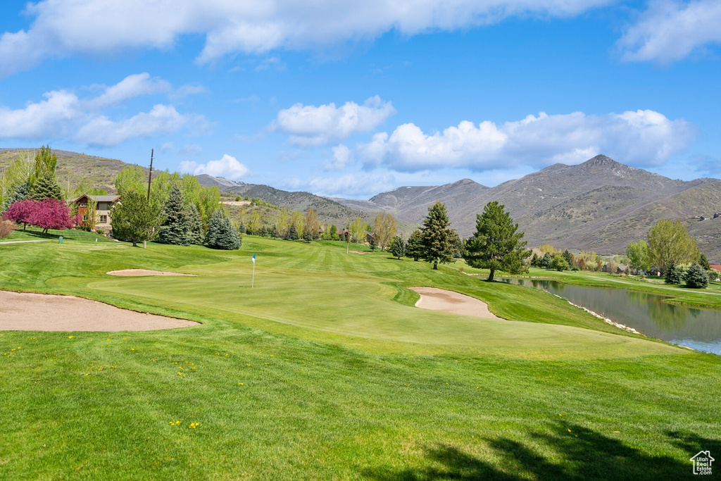 View of community with view of golf course, a water and mountain view, a yard, and an area to practice putting