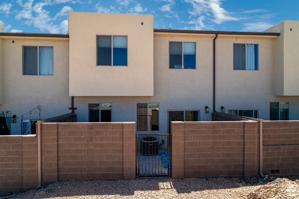 Back of house with fence, stucco siding, a gate, and central air condition unit
