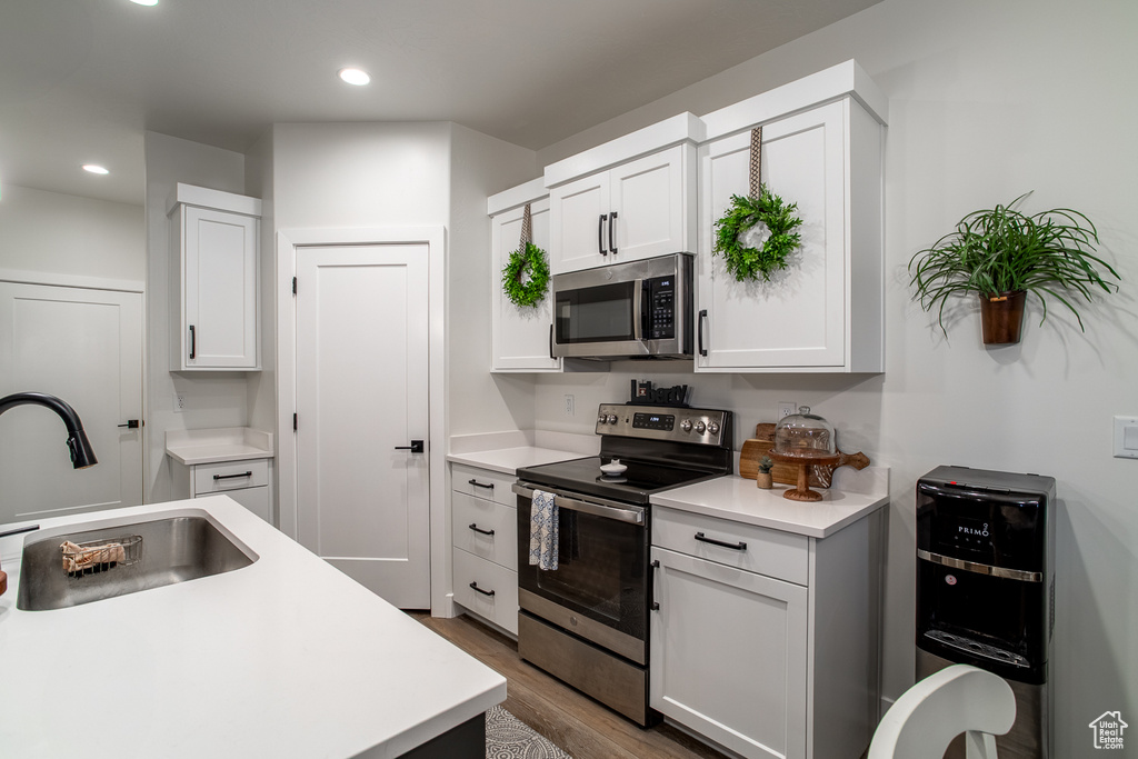 Kitchen featuring appliances with stainless steel finishes, a sink, light countertops, wood finished floors, and recessed lighting