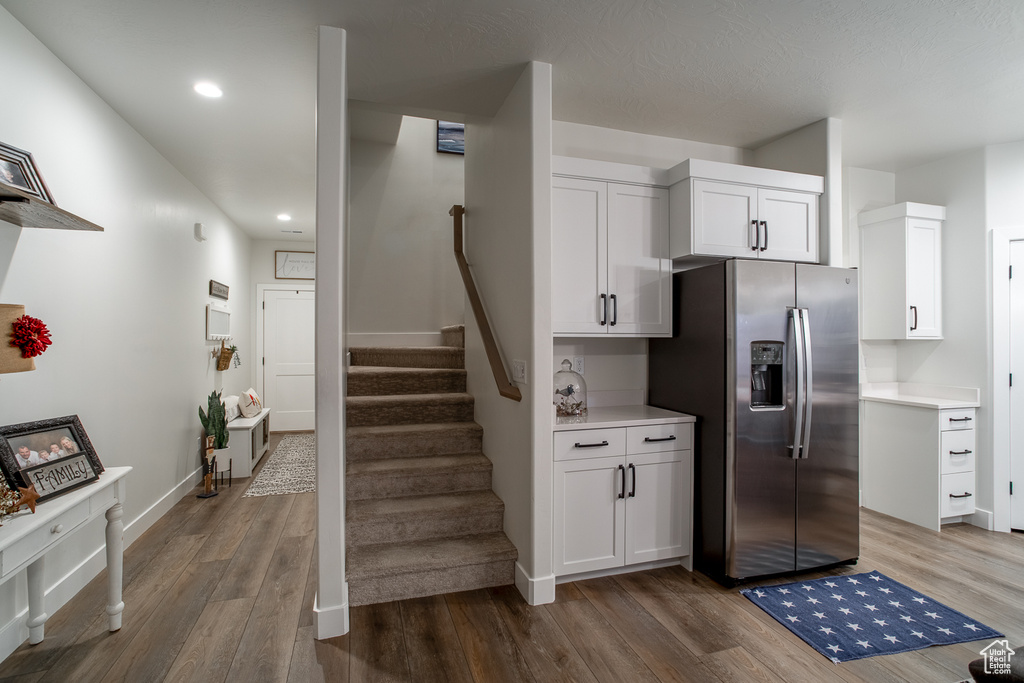 Kitchen with stainless steel fridge with ice dispenser, wood finished floors, white cabinetry, light countertops, and recessed lighting