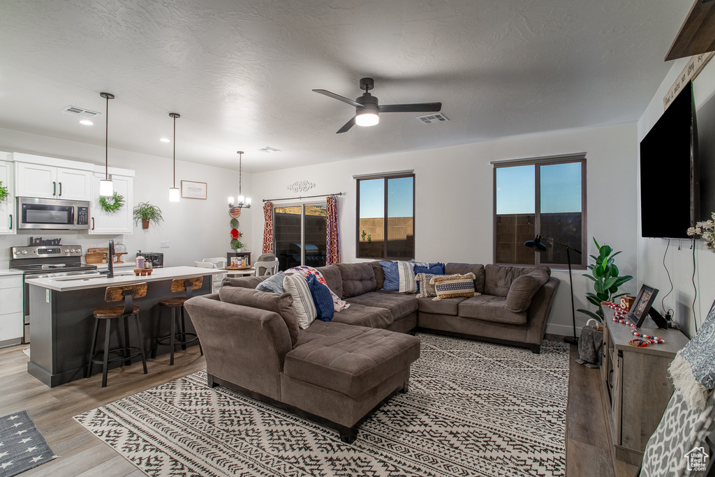 Living area with light wood-style flooring, ceiling fan, a chandelier, and recessed lighting