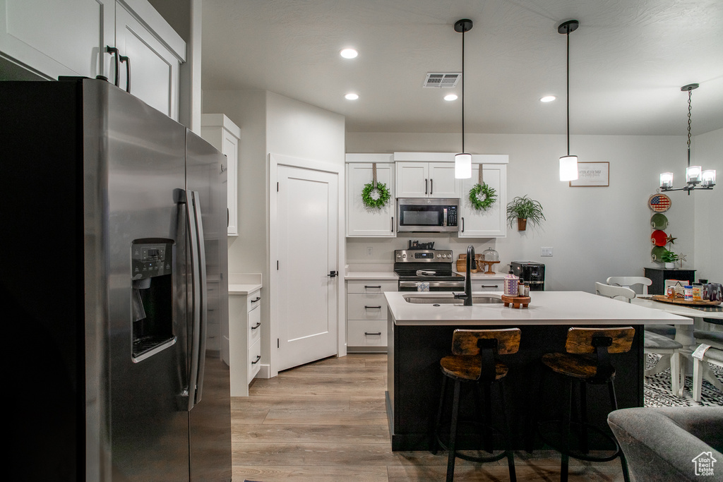 Kitchen featuring stainless steel appliances, light wood-style flooring, light countertops, recessed lighting, and decorative light fixtures