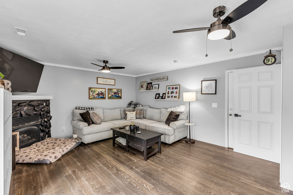 Living area with ceiling fan, wood finished floors, ornamental molding, and a stone fireplace