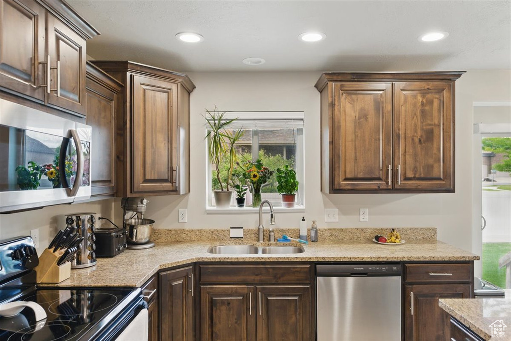 Kitchen featuring stainless steel appliances, a sink, recessed lighting, dark brown cabinets, and light stone counters