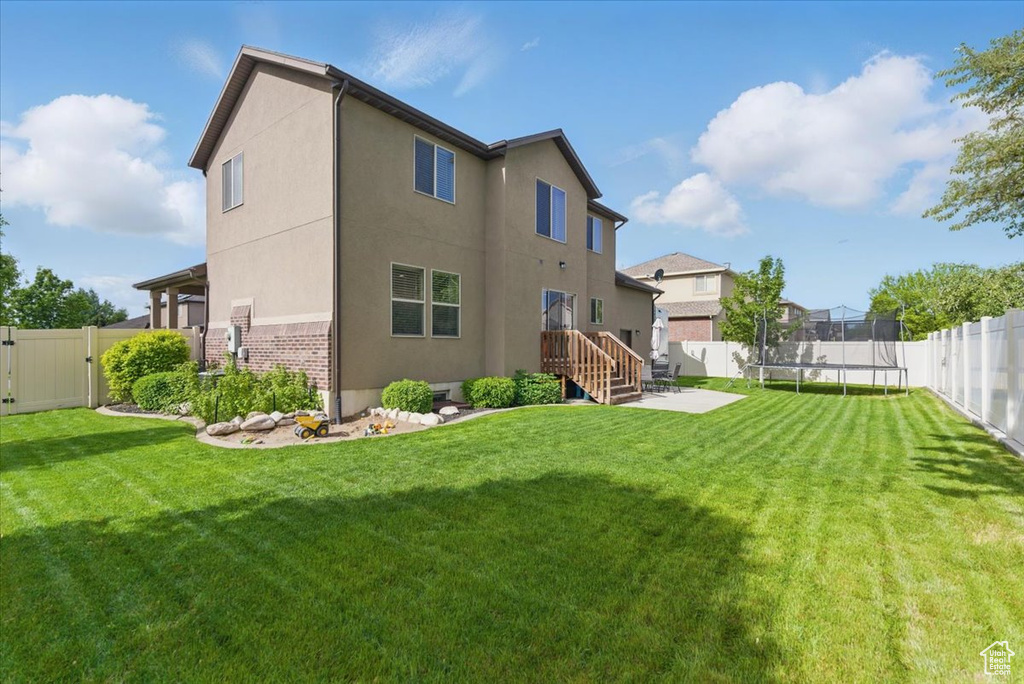Rear view of property featuring a trampoline, stucco siding, a gate, a patio area, and brick siding
