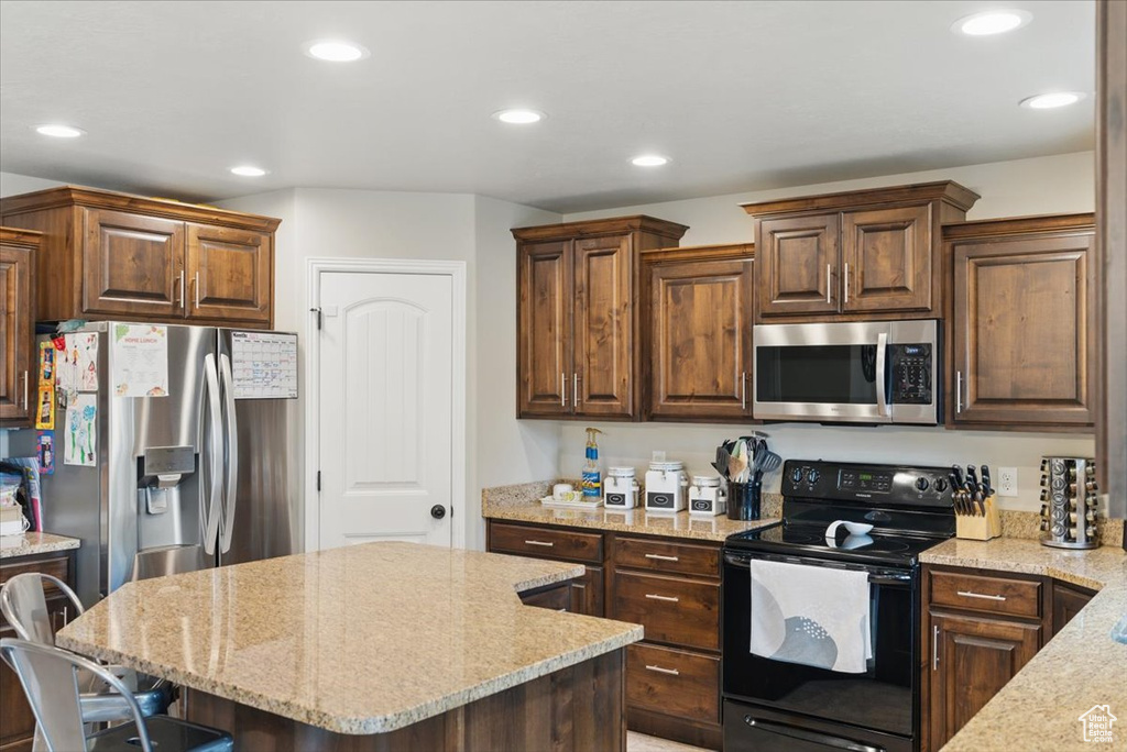 Kitchen featuring stainless steel appliances, light stone countertops, recessed lighting, a kitchen island, and a kitchen bar