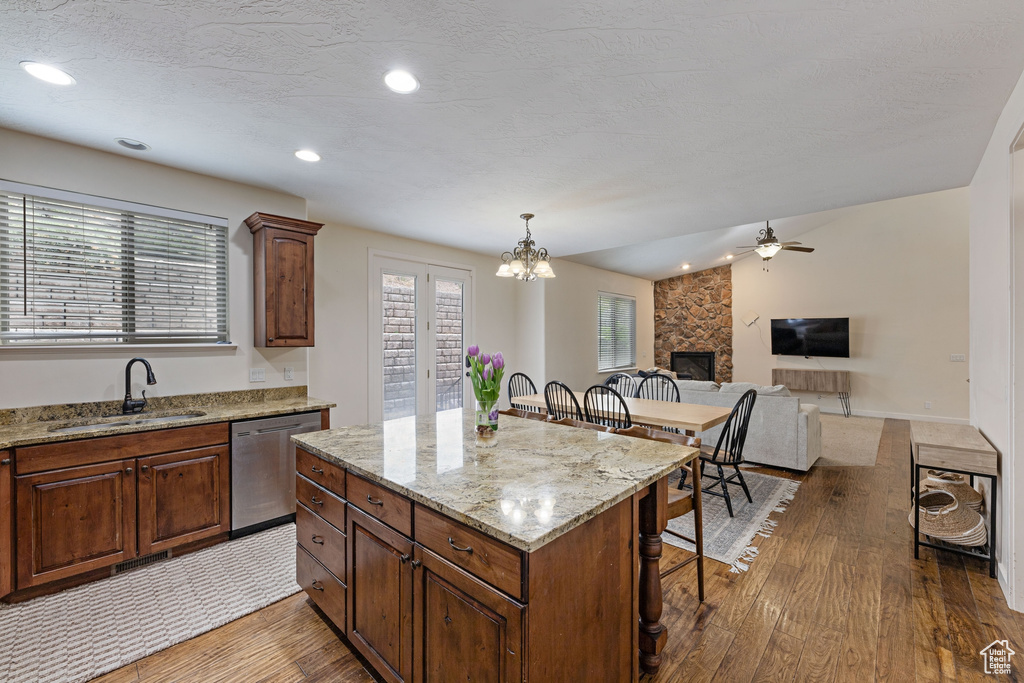 Kitchen featuring a sink, dishwasher, wood finished floors, a breakfast bar area, and a fireplace
