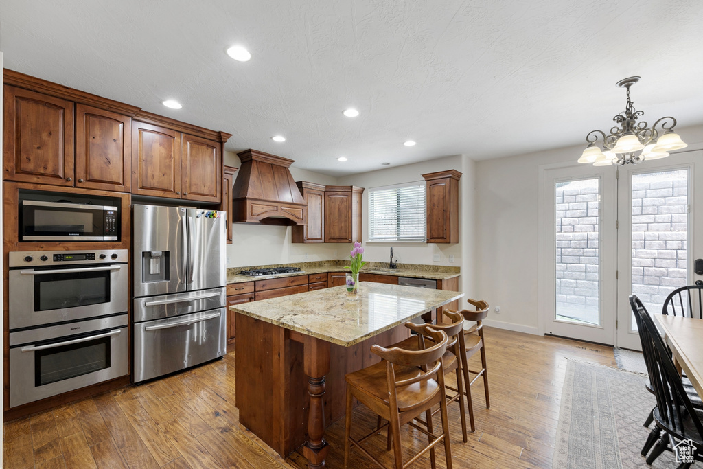 Kitchen with stainless steel appliances, custom range hood, light wood-style flooring, a chandelier, and recessed lighting