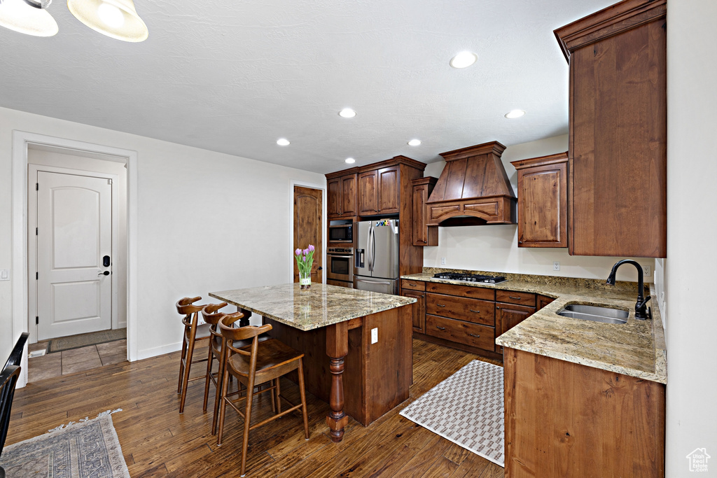 Kitchen featuring custom range hood, a sink, stainless steel appliances, a center island, and dark wood finished floors