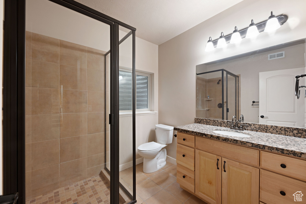 Bathroom with a stall shower, tile patterned floors, toilet, and vanity