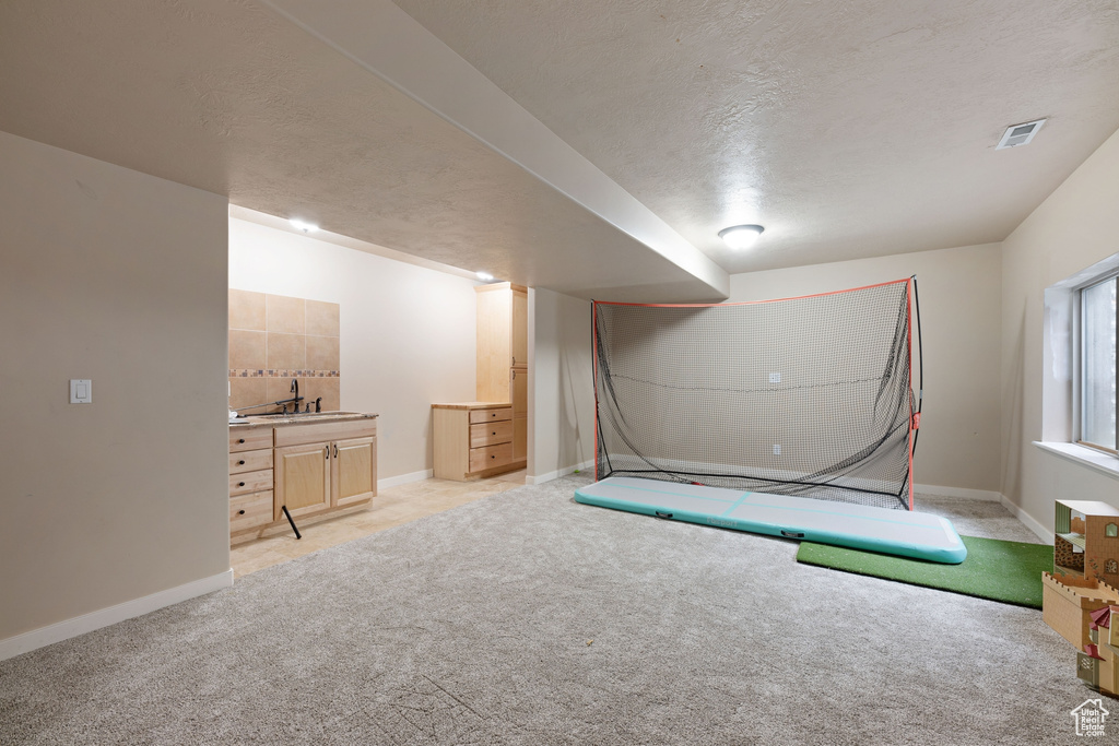 Basement featuring light carpet, baseboards, a textured ceiling, and bar with sink