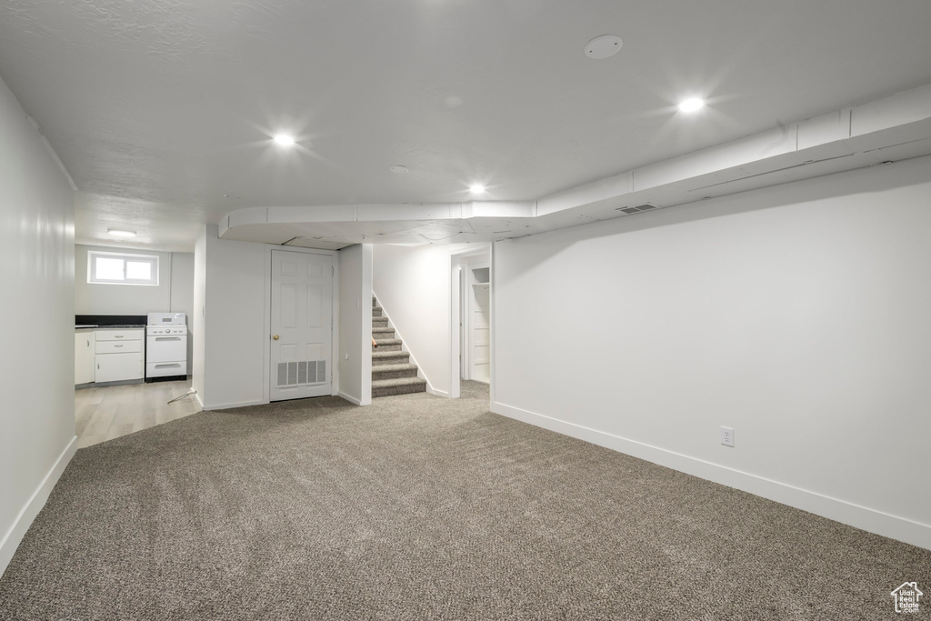 Below grade area with light carpet, baseboards, stairway, and recessed lighting