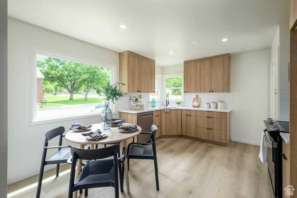 Kitchen with appliances with stainless steel finishes, a sink, light countertops, tasteful backsplash, and light wood-type flooring