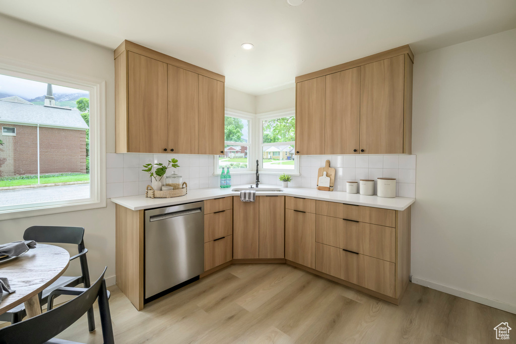 Kitchen with stainless steel dishwasher, a sink, tasteful backsplash, light wood-style flooring, and light countertops
