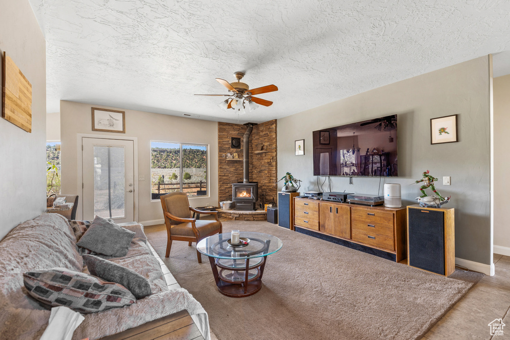 Living area featuring a wood stove, ceiling fan, baseboards, and a textured ceiling