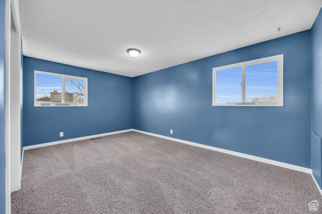 Carpeted spare room featuring a textured ceiling and baseboards