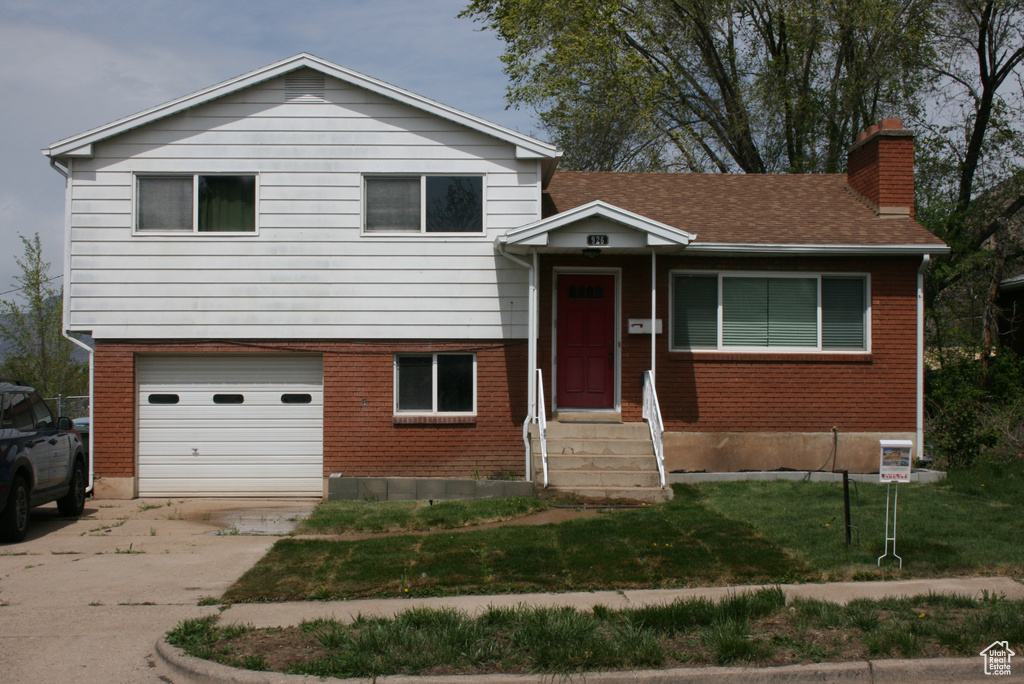 Split level home with a chimney, a garage, brick siding, driveway, and a front yard
