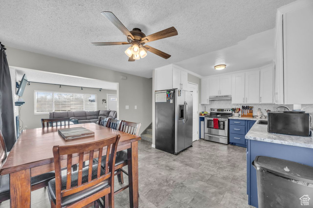 Kitchen featuring appliances with stainless steel finishes, under cabinet range hood, white cabinetry, a ceiling fan, and blue cabinetry