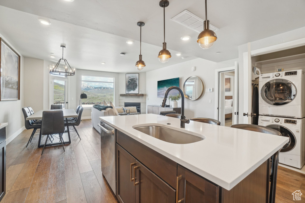 Kitchen with stacked washing machine and dryer, a sink, stainless steel dishwasher, light countertops, and hanging light fixtures