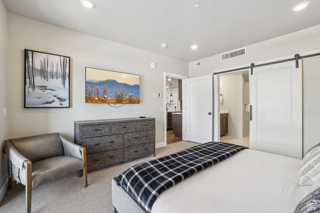 Bedroom with a barn door, light colored carpet, recessed lighting, ensuite bath, and baseboards