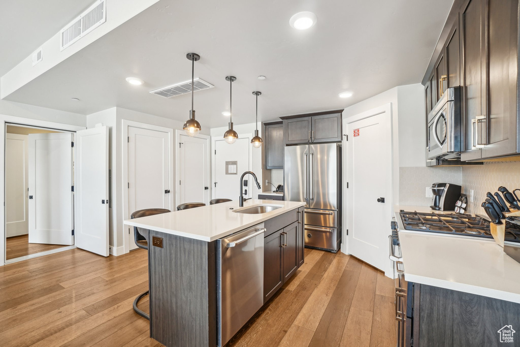 Kitchen featuring a sink, premium appliances, light wood-style flooring, a breakfast bar, and recessed lighting