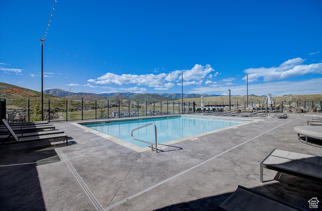 Community pool with fence, a mountain view, and a patio area