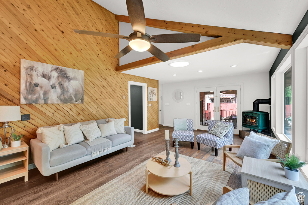 Living area with a wood stove, wood finished floors, beam ceiling, a ceiling fan, and wood walls
