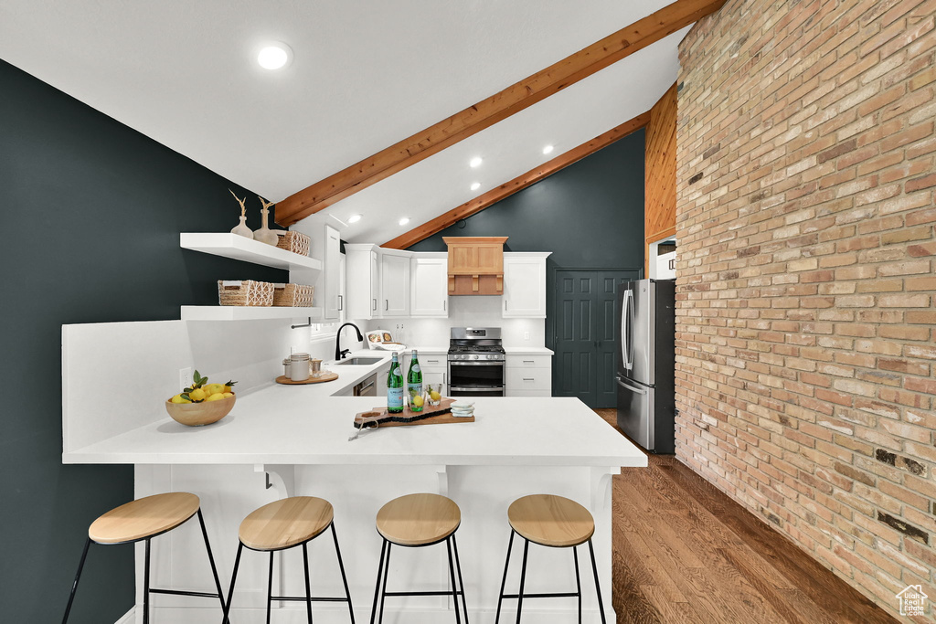 Kitchen featuring appliances with stainless steel finishes, open shelves, a peninsula, beamed ceiling, and light wood finished floors