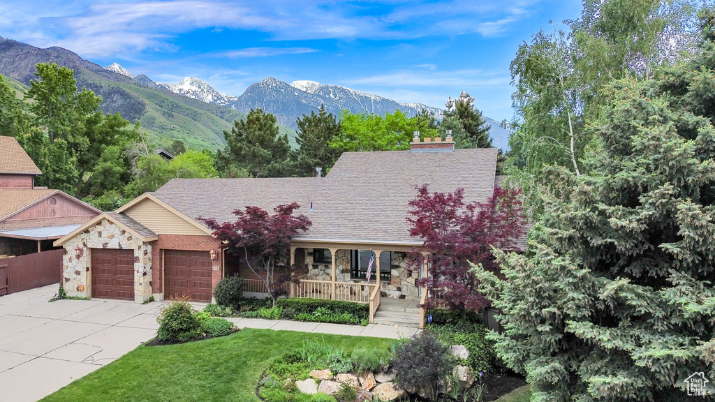 View of front of home featuring a garage, stone siding, a porch, a mountain view, and driveway
