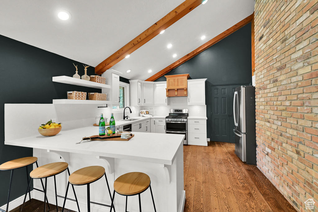 Kitchen with appliances with stainless steel finishes, a sink, a peninsula, beam ceiling, and light wood-type flooring