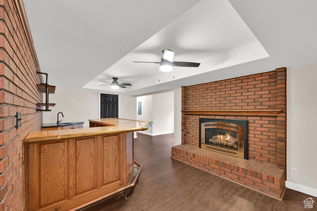 Kitchen with a tray ceiling, a fireplace, a sink, dark wood-style flooring, and baseboards