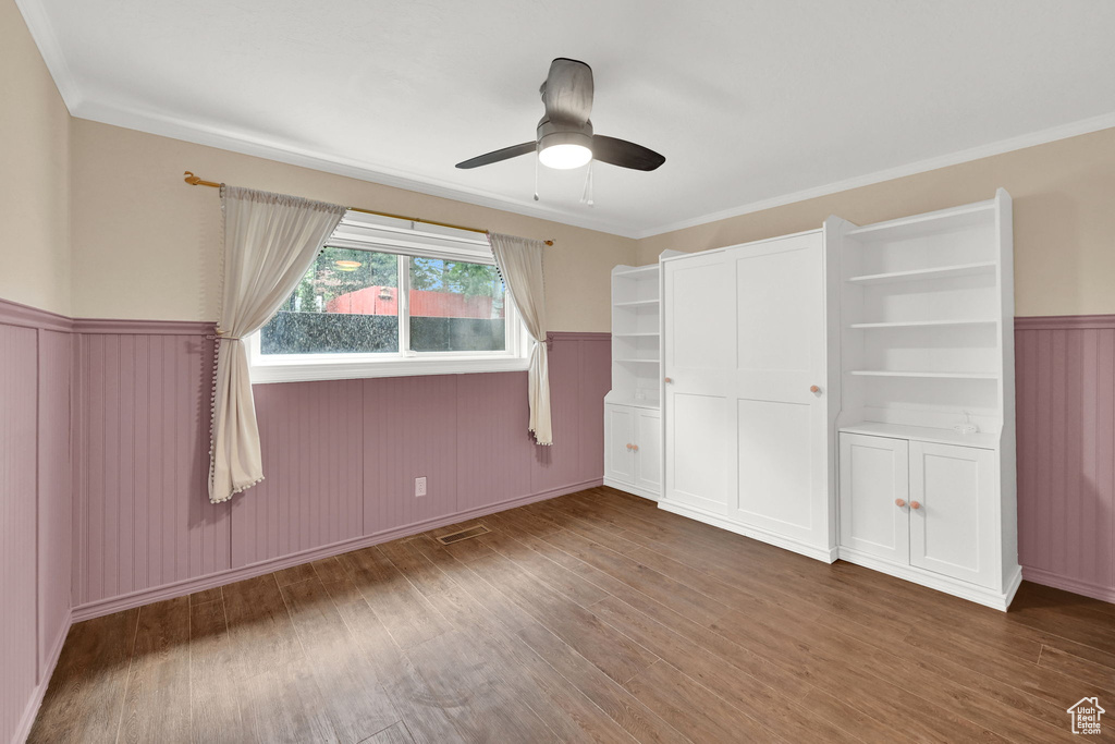 Unfurnished bedroom with wood finished floors, wainscoting, ornamental molding, and a ceiling fan