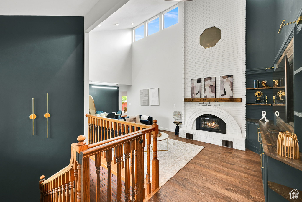 Living room with a high ceiling, a brick fireplace, and wood finished floors