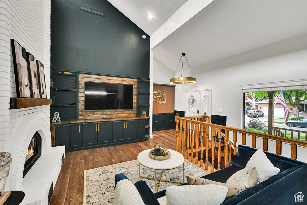 Living room with a brick fireplace, wood finished floors, high vaulted ceiling, and recessed lighting