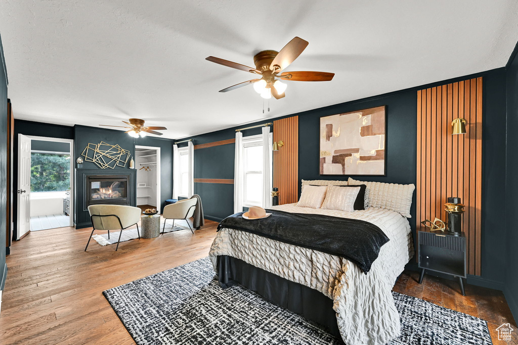 Bedroom with a glass covered fireplace, wood finished floors, a ceiling fan, and baseboards