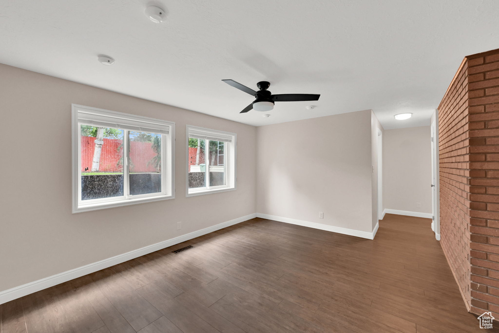 Spare room featuring dark wood finished floors, ceiling fan, baseboards, and brick wall