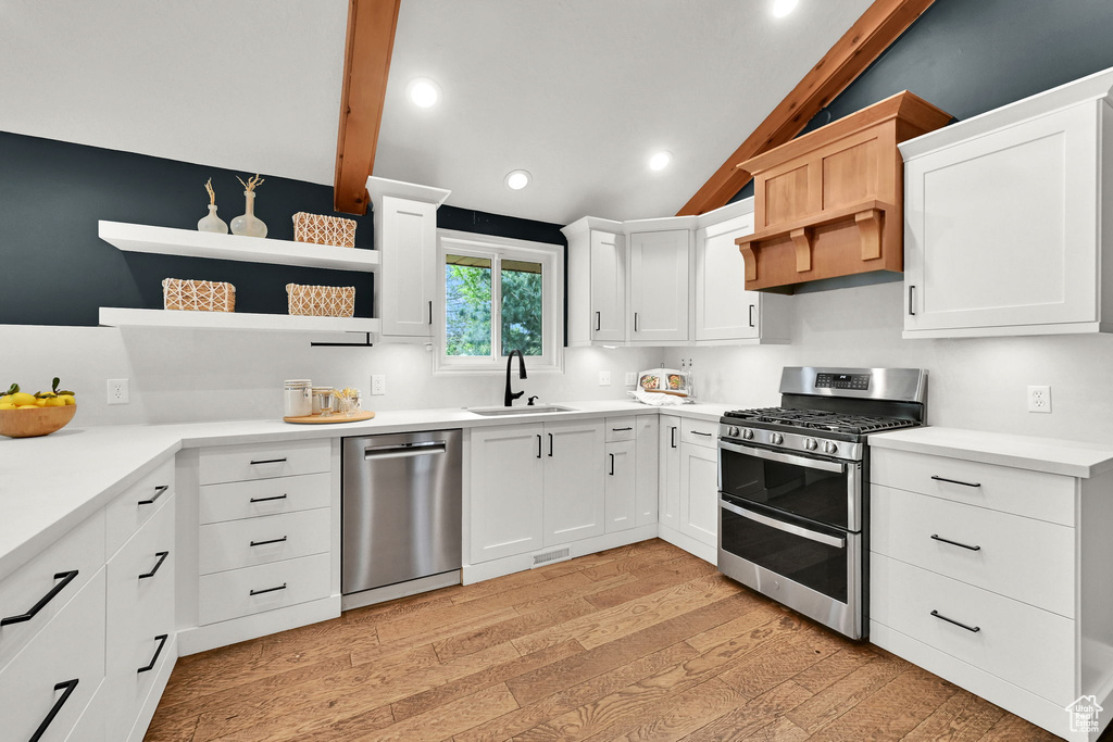 Kitchen featuring appliances with stainless steel finishes, a sink, open shelves, light wood-style flooring, and lofted ceiling