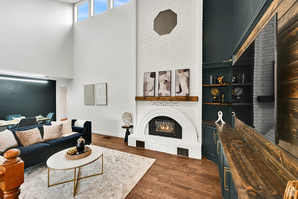 Living room featuring a high ceiling, a brick fireplace, dark wood-style floors, and baseboards