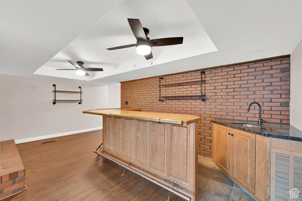 Indoor wet bar with brick wall, a raised ceiling, ceiling fan, baseboards, and wood finished floors