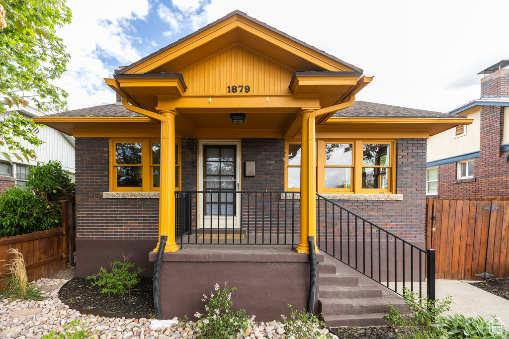 View of front of house with brick siding, fence, and roof with shingles