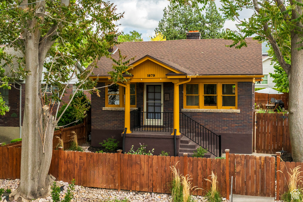 Bungalow with brick siding, a chimney, and a shingled roof
