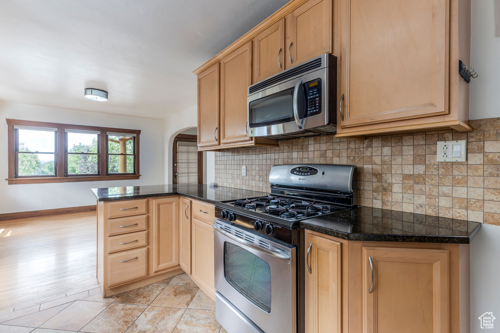 Kitchen with appliances with stainless steel finishes, arched walkways, a peninsula, and dark countertops