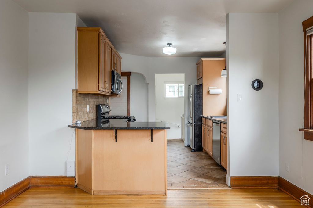 Kitchen featuring stainless steel appliances, a peninsula, a kitchen bar, light wood-type flooring, and baseboards