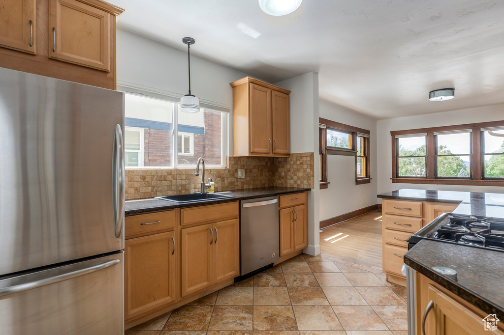 Kitchen with stainless steel appliances, a sink, decorative backsplash, baseboards, and pendant lighting
