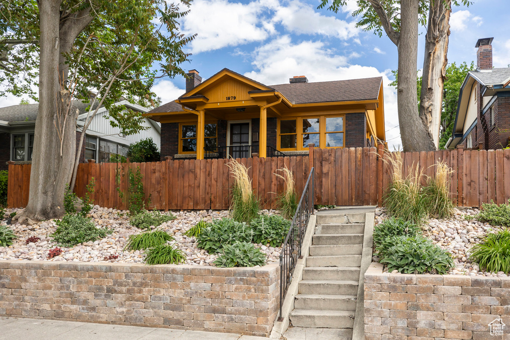 Bungalow with a chimney, a fenced front yard, brick siding, and stairs
