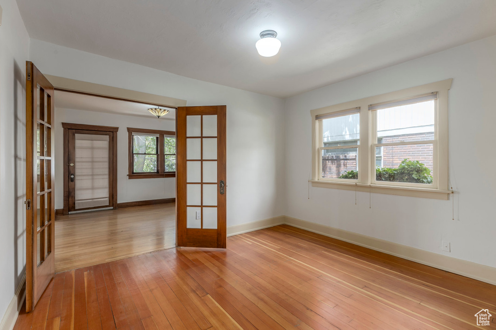 Unfurnished room with french doors, light wood-style floors, and baseboards
