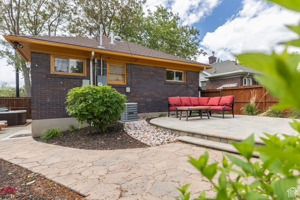 Rear view of house featuring an outdoor hangout area, a patio area, fence, and brick siding