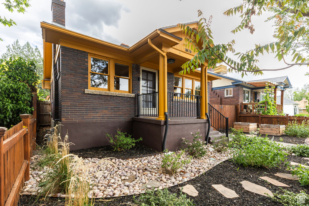 View of front of house with brick siding, a chimney, fence, and covered porch