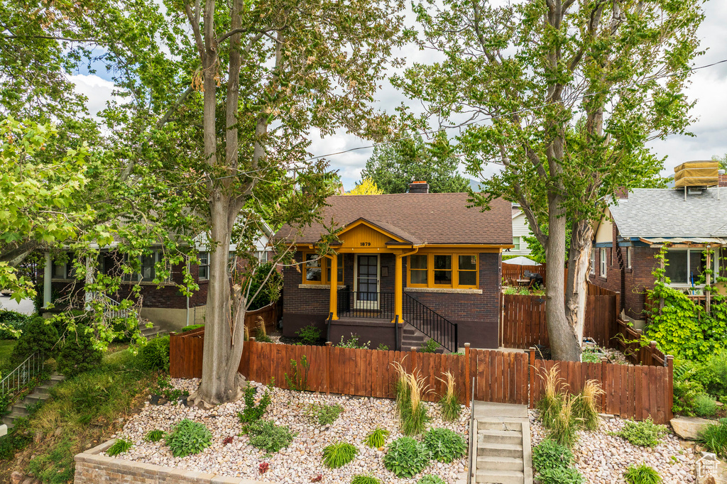 View of front of property featuring a fenced front yard, brick siding, a chimney, roof with shingles, and a gate